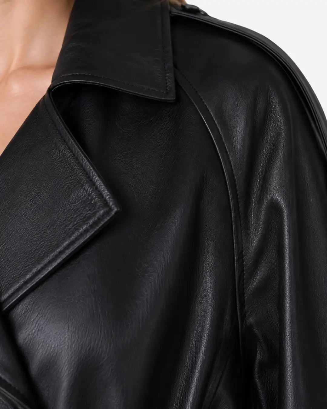 Close-up of a black leather jacket with a wide collar and shoulder seam, worn by a model against a light gray background.